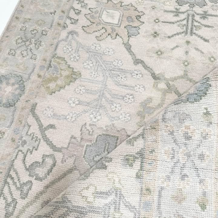 A close-up view of a Modern Oushak rug featuring a geometric pattern in green, blue, and beige tones.