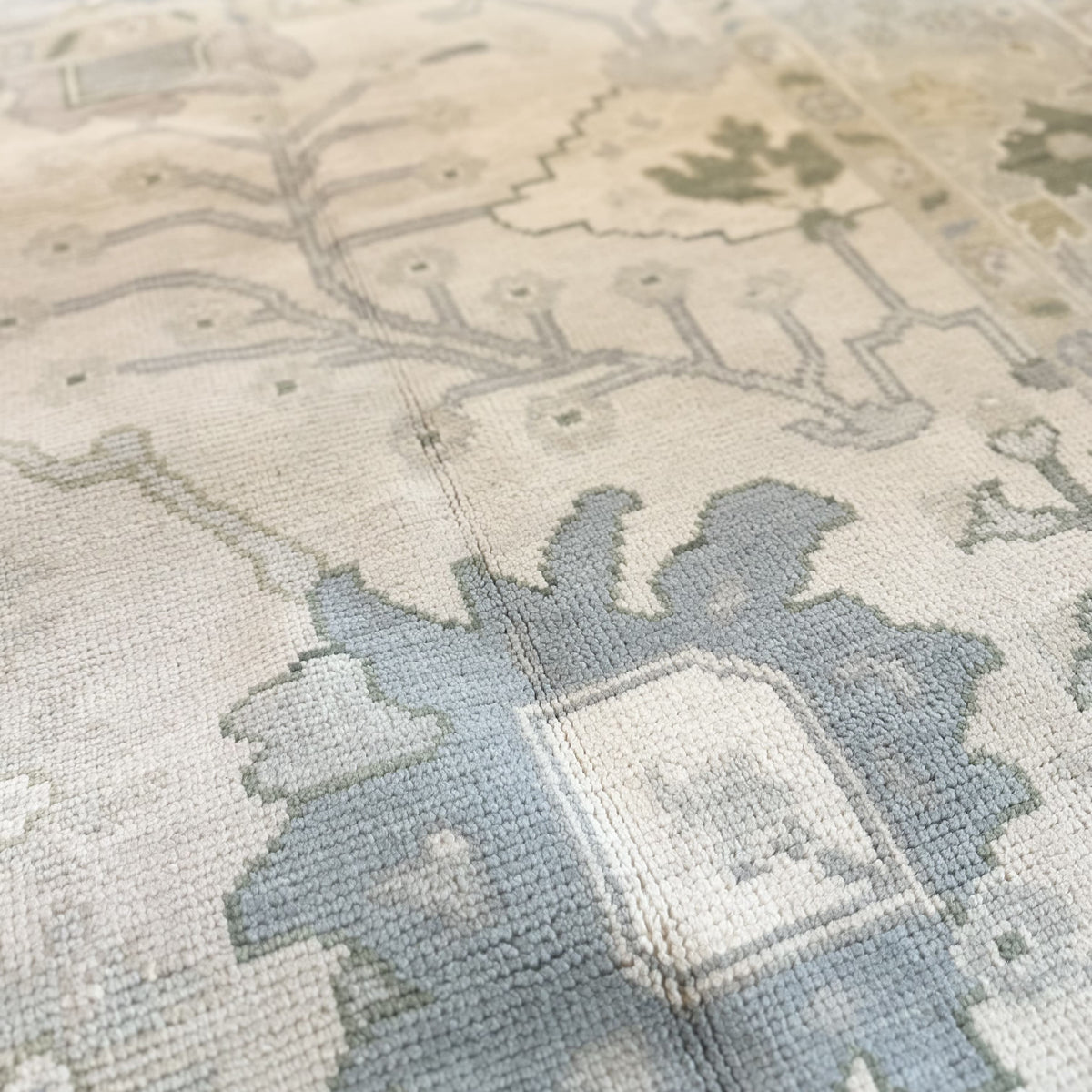A close-up view of a Modern Oushak rug featuring a geometric pattern in green, blue, and beige tones.