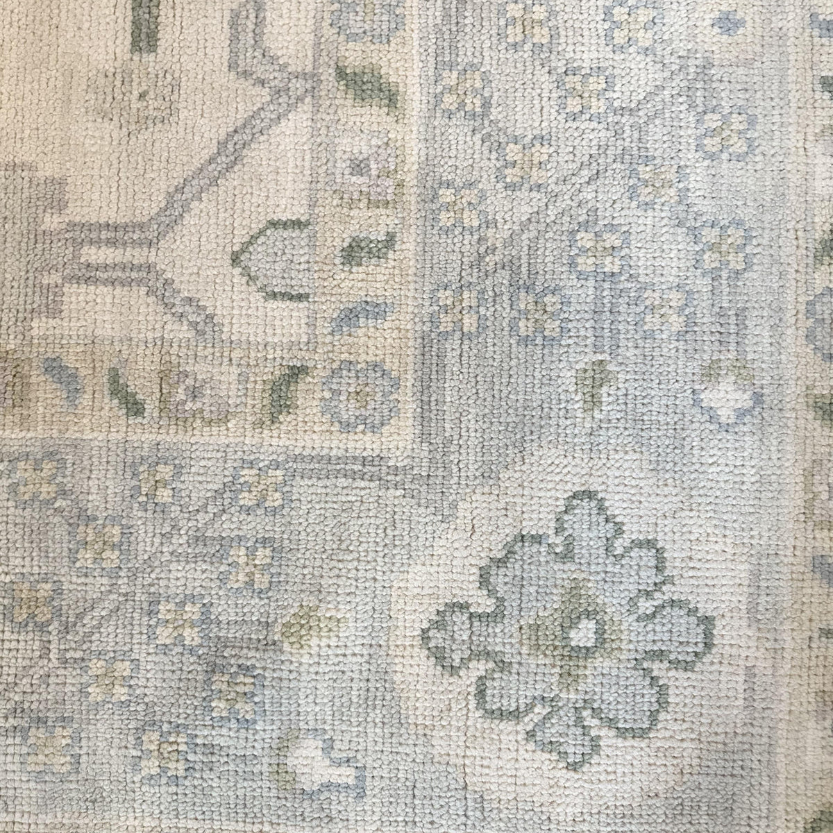 A close-up view of a Modern Oushak rug featuring a geometric pattern in green, blue, and beige tones.