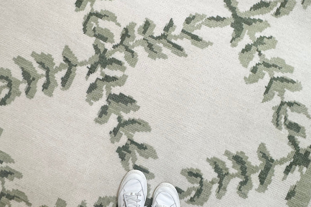Person wearing white sneakers and striped pants standing on a green and beige patterned rug in a laurel floral motif.