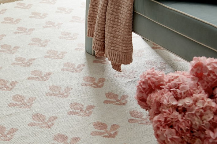 Patterned rug with floral design, bench, and pink flowers in a room.