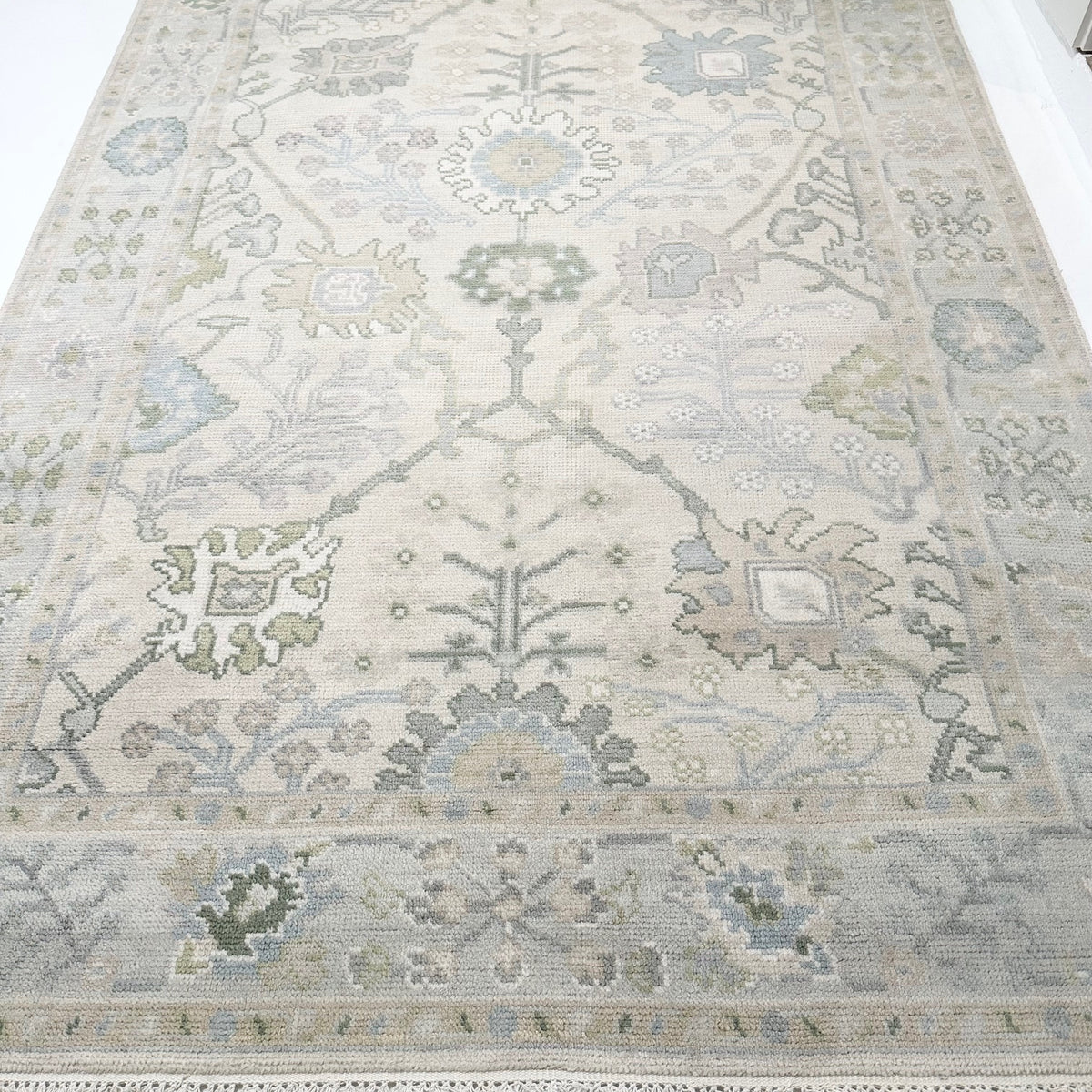 A close-up view of a Modern Oushak rug featuring a geometric pattern in green, blue, and beige tones.