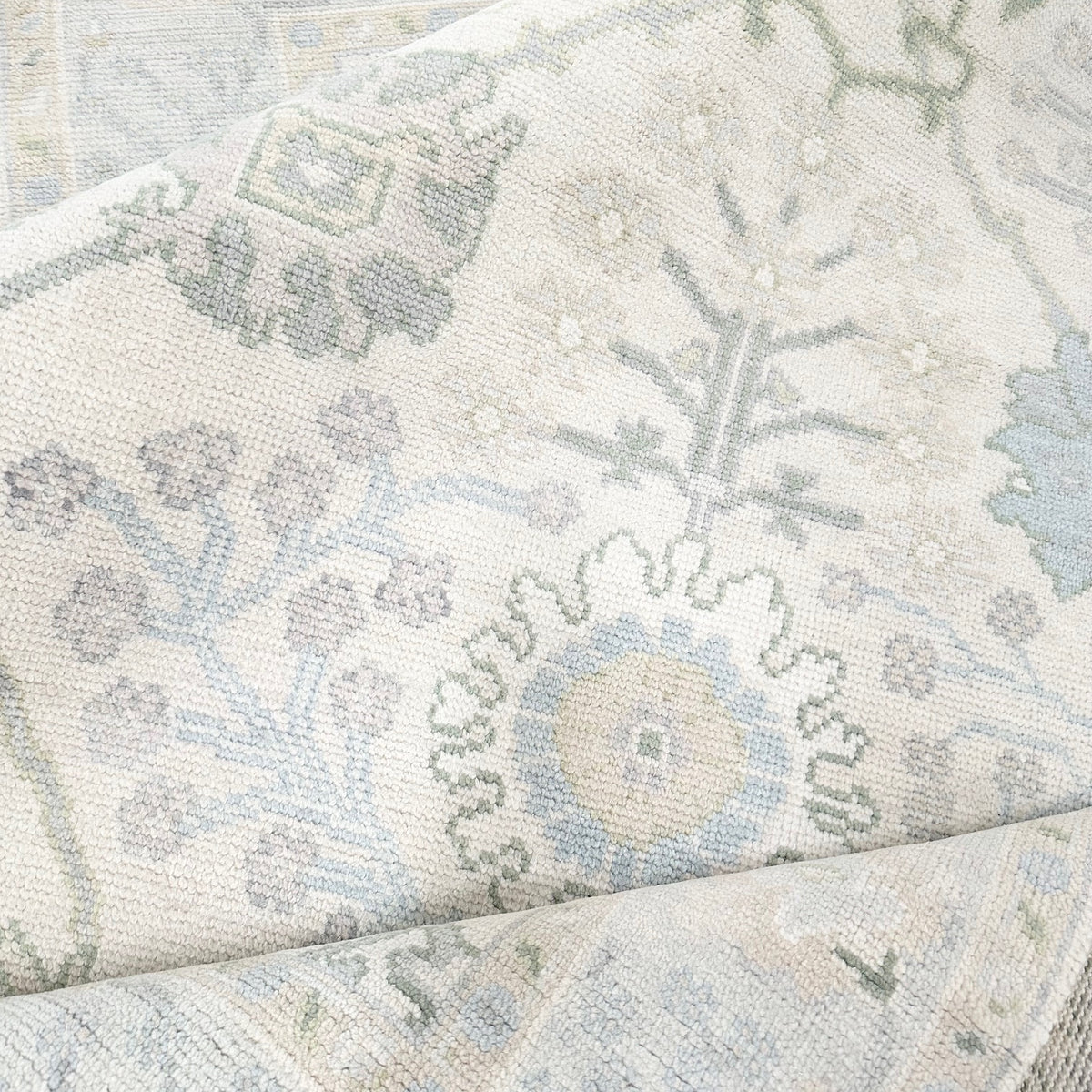 A close-up view of a Modern Oushak rug featuring a geometric pattern in green, blue, and beige tones.