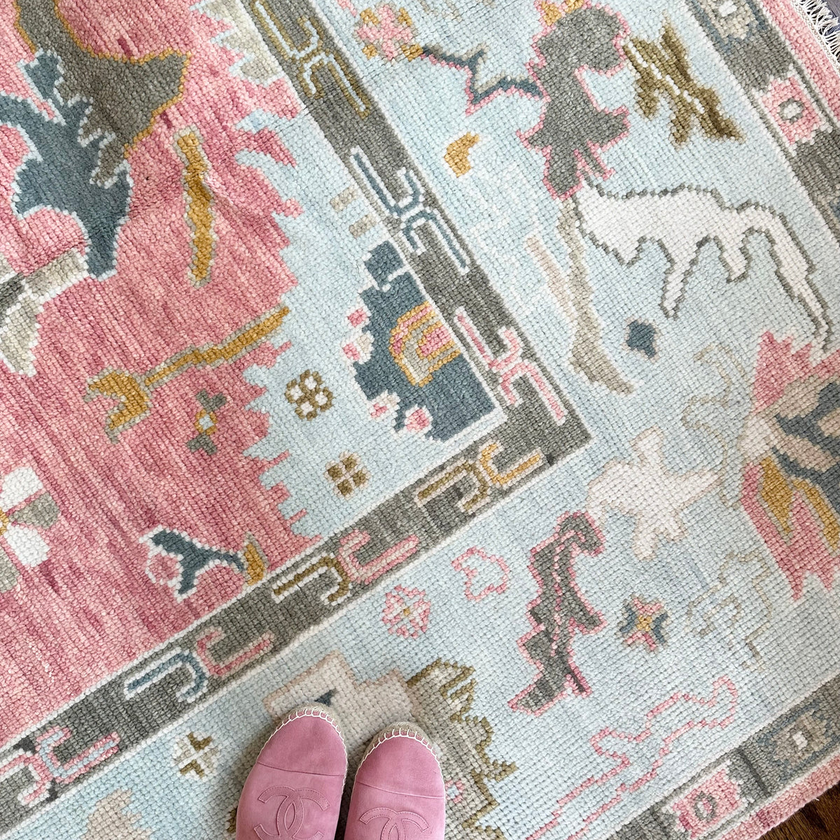 A person standing on a pink and beige geometric patterned rug, with their feet visible wearing pink slippers.