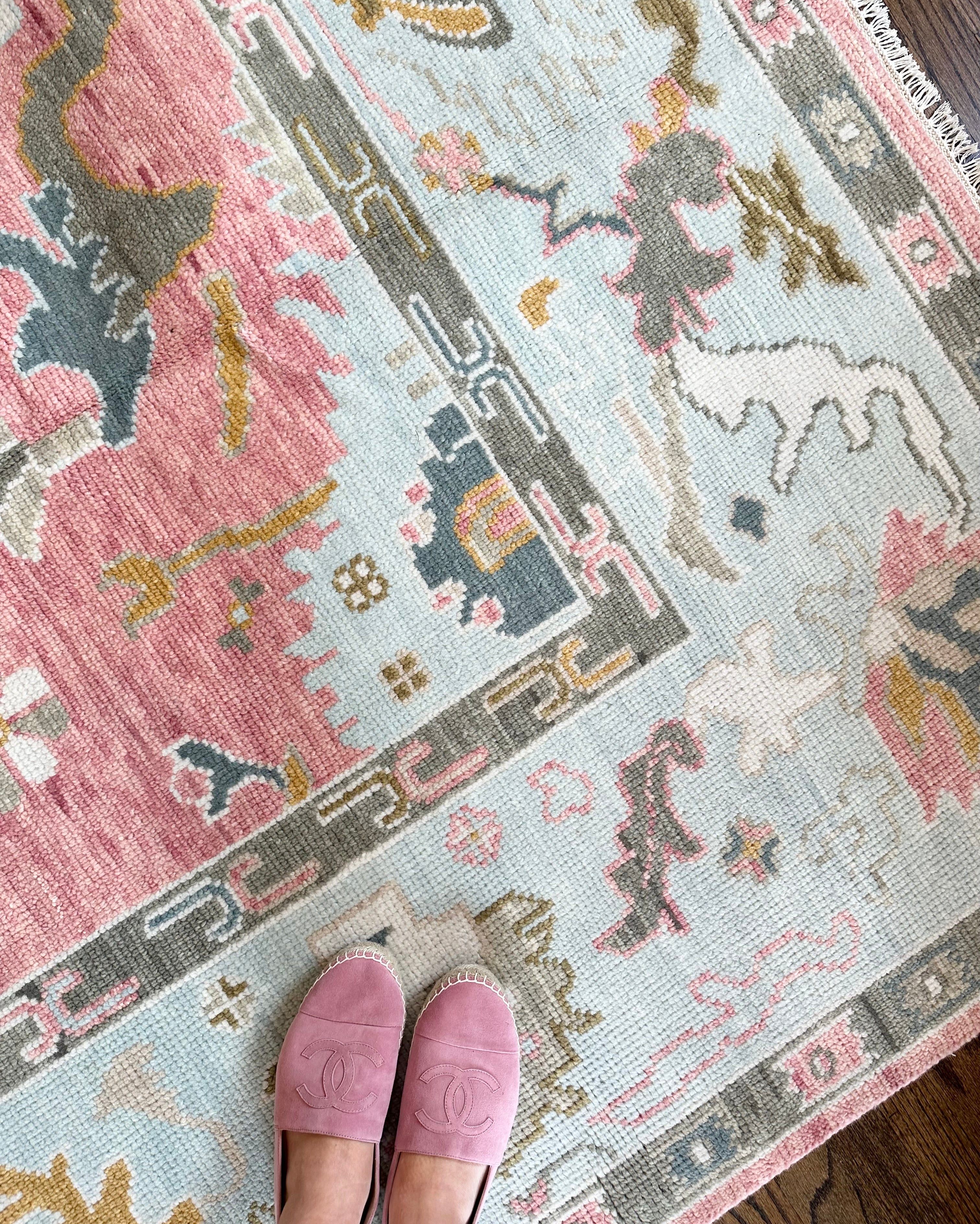 A person standing on a pink and beige geometric patterned rug, with their feet visible wearing pink slippers.