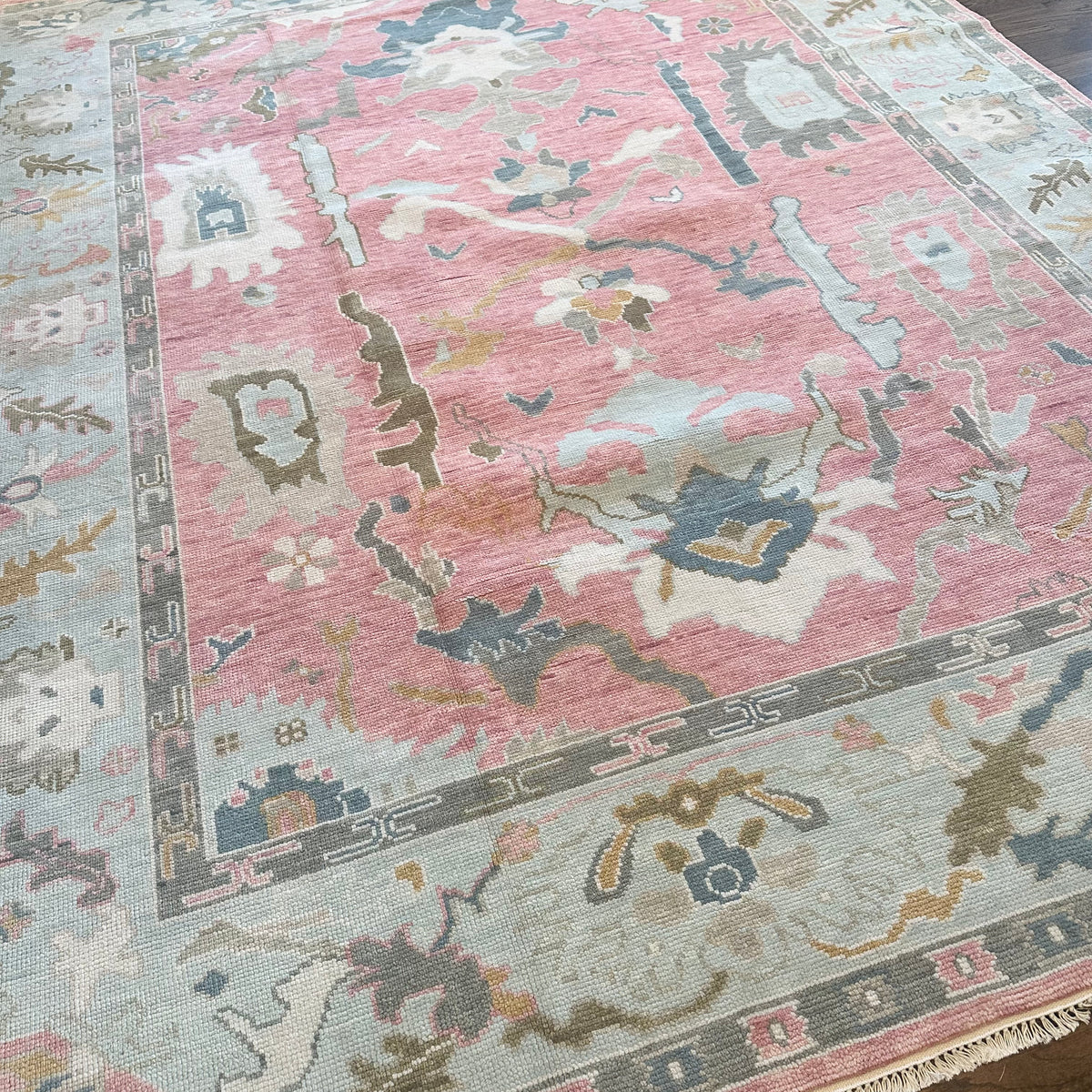 A close-up view of a colorful modern Oushak rug featuring floral patterns in multiple colors including pink, blue, green, and taupe.